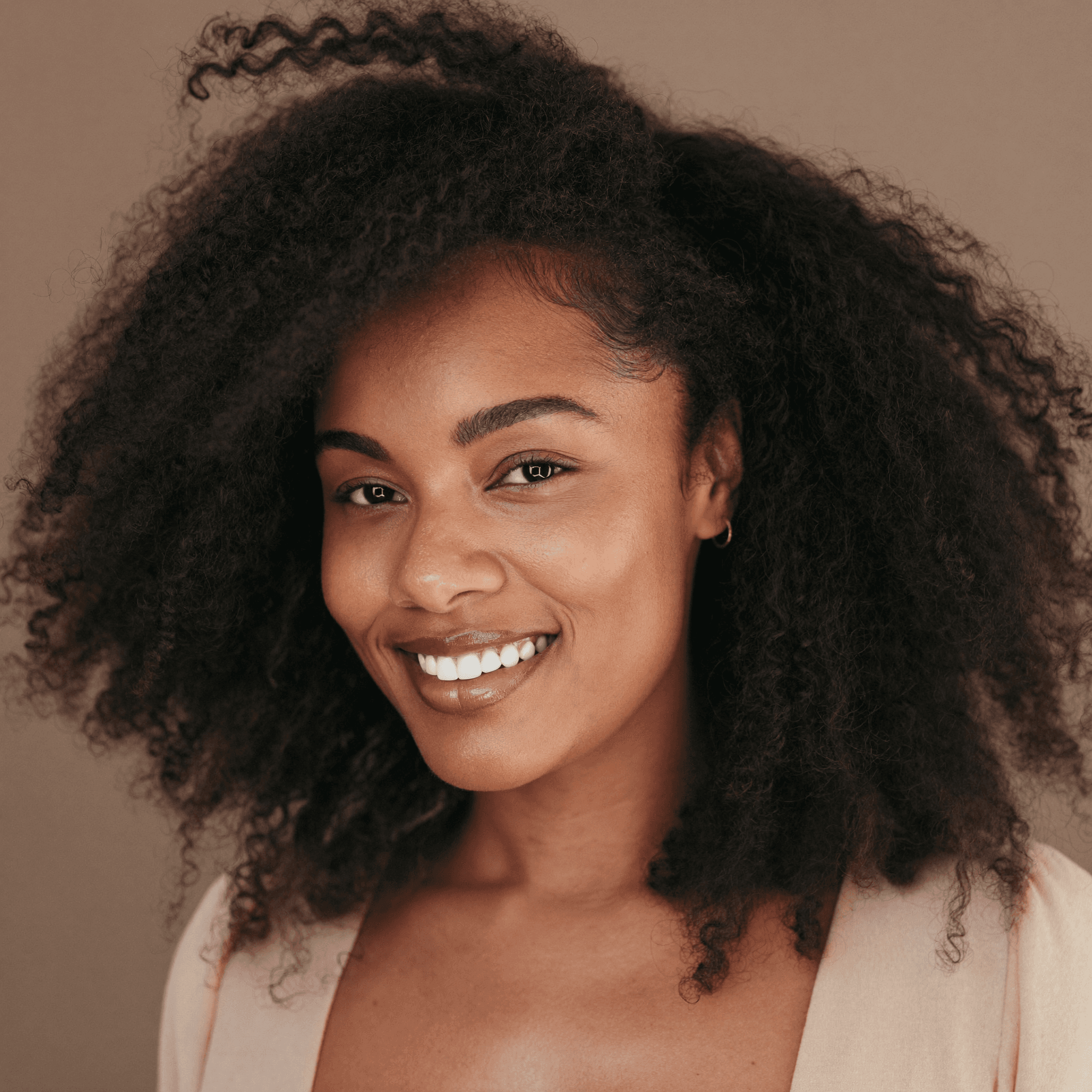 Smiling Black woman with voluminous curly hair and glowing skin against a tan background.