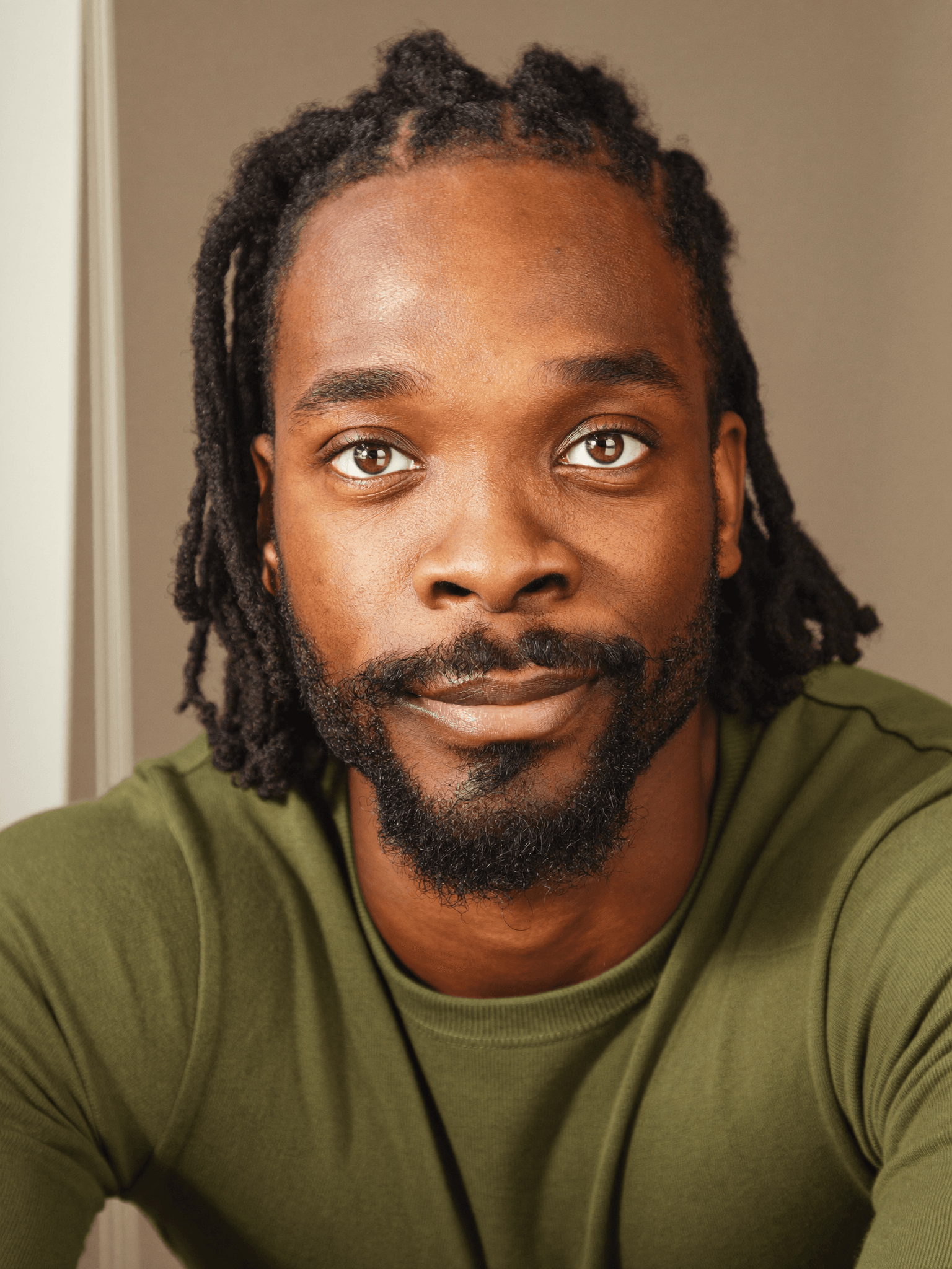 Close-up of a Black man with dreadlocks and a beard, wearing an olive green shirt.